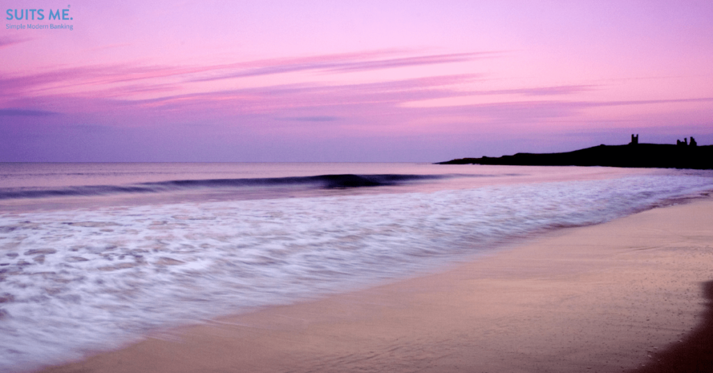 Picturesque image of a shoreline in Northumbria, UK with purple skyline at sunset. cliffs and an old castle in the background