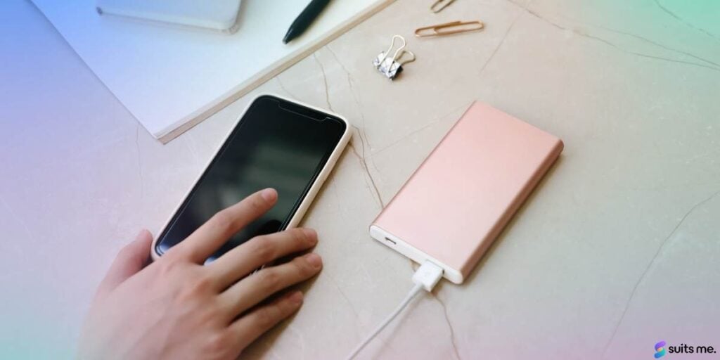 Mobile phone on a desk being charged with a woman's hand reaching for the phone to log into their mobile banking app