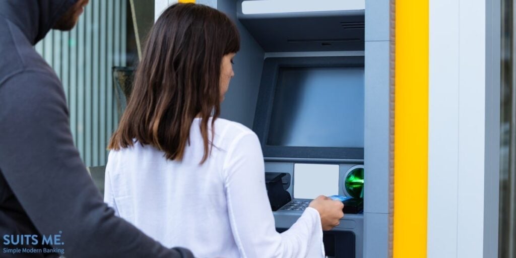 Rear View Of A Thief Trying to View Woman's Debit Card Pin Number Whilst She's Using ATM Machine