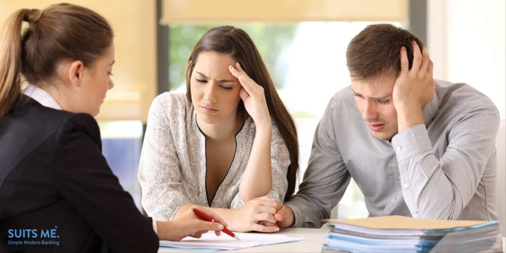 Banker explaining conditions of a document with bad news to a couple of worried customers at a bank