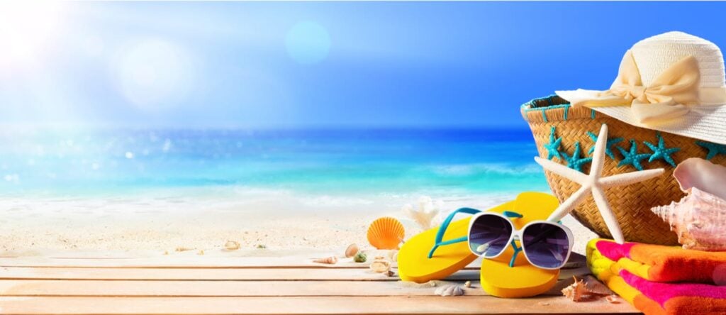 Beach scene with sand, sea and sun. Image of straw sunhat and typical items you take to the beach