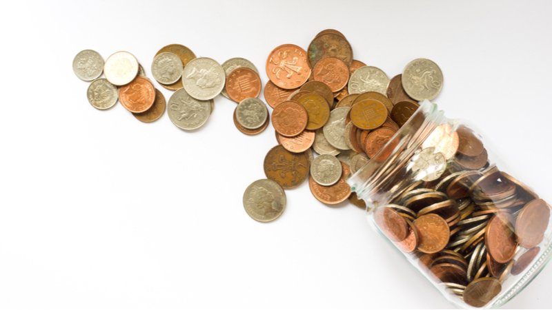 Low Denomination British Currency spilling out of a glass jar that's fallen over