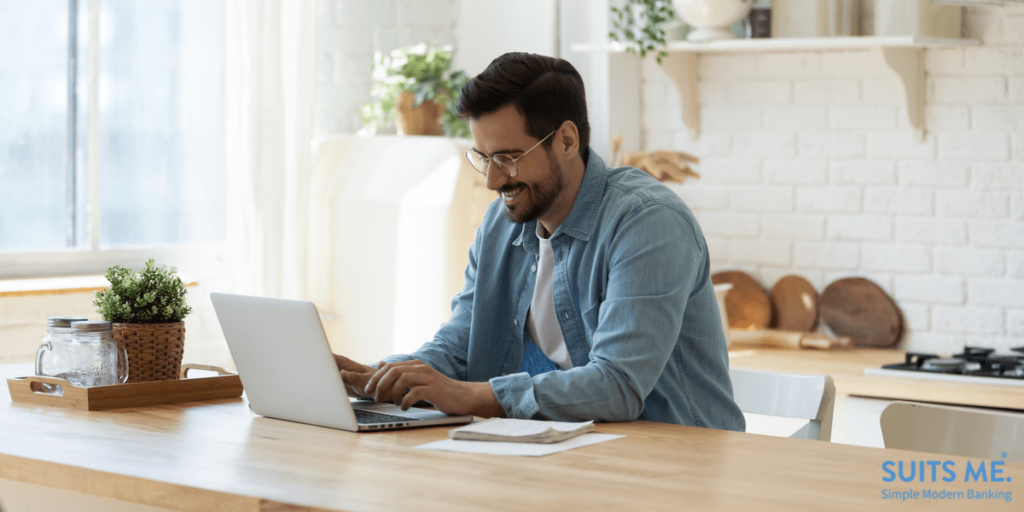 happy young male using on laptop using online banking service in modern kitchen