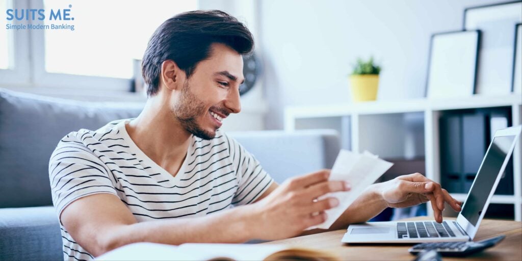 Happy man setting up a standing order to pay bills on his laptop in living room