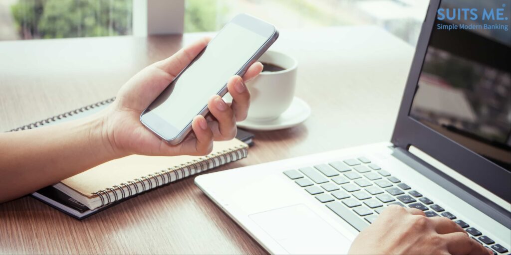 Close Up of a woman's hands using mobile phone and laptop computer to manage both online and mobile banking.