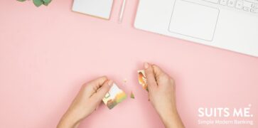 Broken debit card in women's hands. White Laptop, pen and notepad on desk with pink background. plastic free payment method concept.