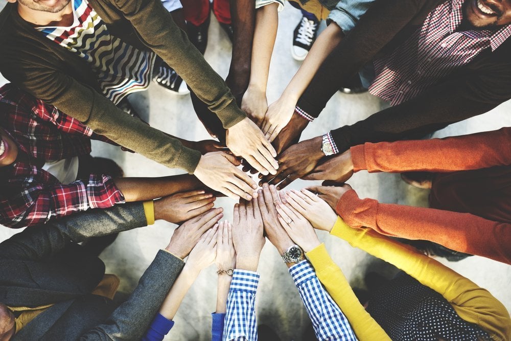 Staff stood in a circle all with their hands in about to cheer. Moral in the workplace concept