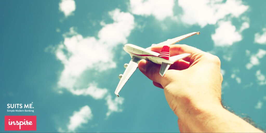 close up photo of man's hand holding toy airplane against blue sky with clouds