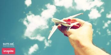 close up photo of man's hand holding toy airplane against blue sky with clouds