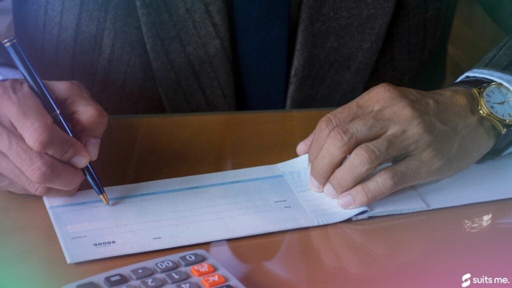 Businessman hand writing and signing white empty bank cheque to pay employees with calculator on desk. Payment by cheque, payroll concept