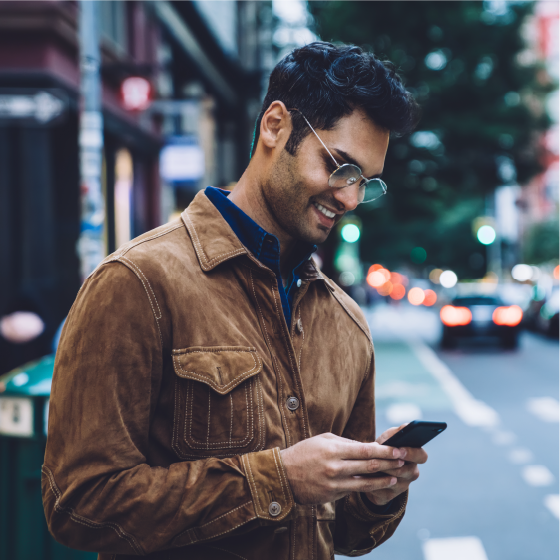 Person duke buzëqeshur ndërsa përdor një telefon inteligjent në një rrugë qyteti