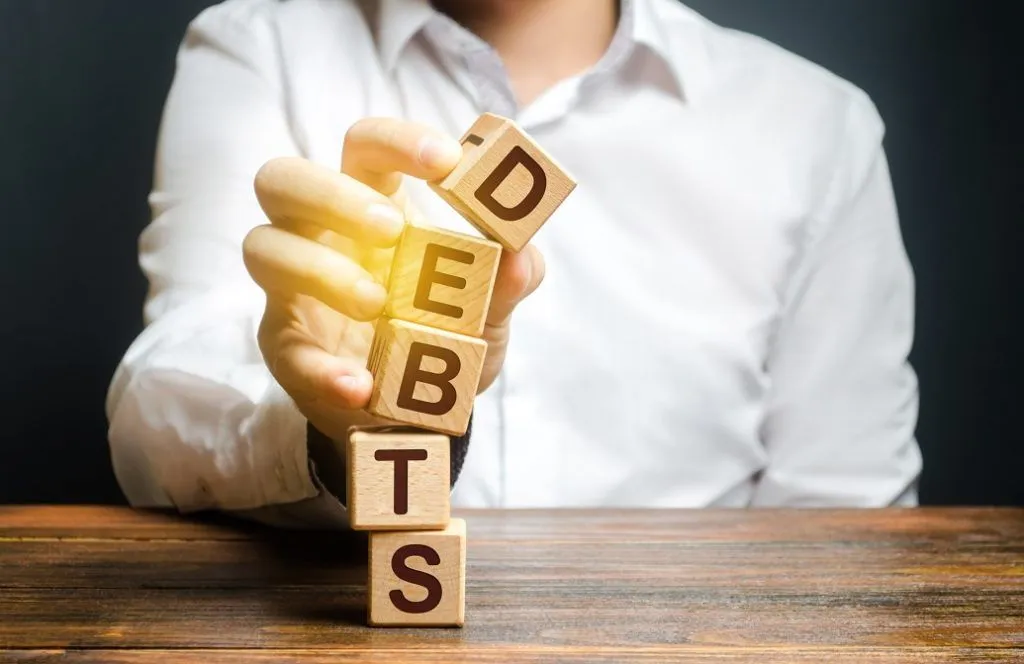 MAN HOLDING WOODEN BLOCKS SPELLING DEBT